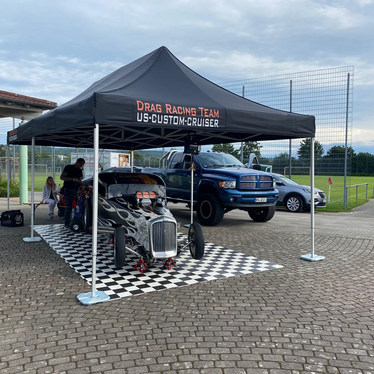 Schwarzer 8x4-Faltpavillon mit Drag Racing Team-Logo bedeckt einen flammenden Oldtimer und wird mit Ecotent-Pavillongewichten am Boden befestigt