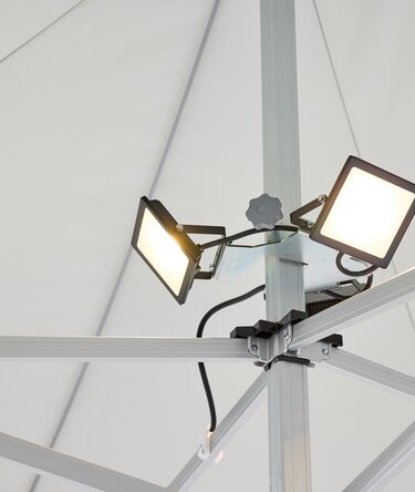 The LED spotlight, consisting of 3 spots, is mounted on the central pole of the folding gazebo. The LED spotlight is on.