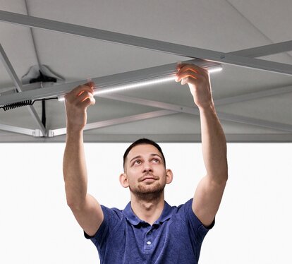 Der Mann bringt die LED-Leisten am Faltpavillon an.