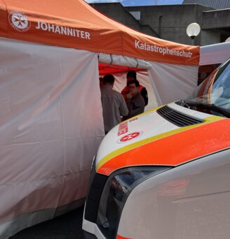 Auf einer gepflasterten Fläche steht ein bedruckter Faltpavillon mit weißen Seitenwänden und orangem Dach von Ecotent der Serie E1 in der Größe 8 x 4 Meter.