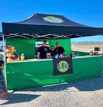 Auf einem Markt steht ein grün-schwarzer, bedruckter Ecotent Faltpavillon Serie E2 der Größe 4,5 x 3 Meter mit Seitenwänden mit Tür und Counter von Ol 6 Six. 